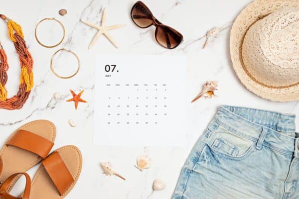 Flat lay with calendar for July with summer holidays fashion accessories