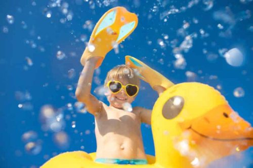 Child having fun on summer vacation. Kid jumping in swimming pool. Low angle view portrait of boy against water splash. Spring break!