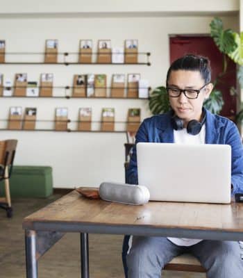 Male Japanese professional sitting at a table in a co-working space, using laptop computer.