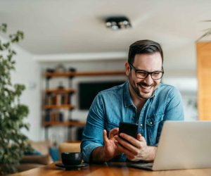 Portrait of a happy man with smart phone and laptop, indoors.